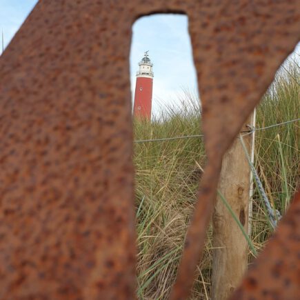 Door een "V" in metaal heen heb je uitzicht op de vuurtoren van Texel